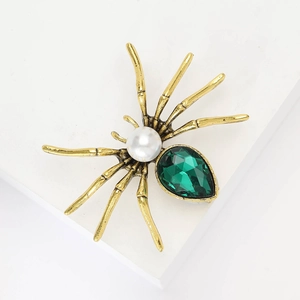 Spider brooch with golden alloy, white pearl head, and green teardrop crystal on white stand