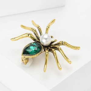 Exquisite vintage gold spider brooch with green gemstone and pearl on a white pedestal