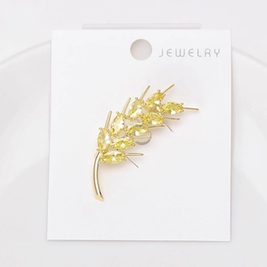 Macro detail of golden wheat ear brooch with yellow zircon stones on jewelry display card