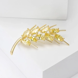 Elegant gold wheat brooch with sparkling zircons on minimalist geometric white background