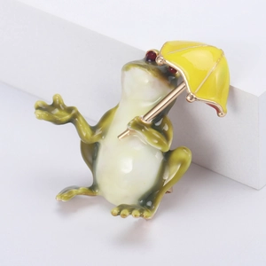 Vue détaillée d'une broche en émail grenouille verte avec parapluie jaune sur socle blanc