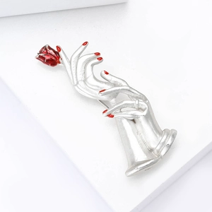 Detail of silver enamel brooch featuring delicate hands holding a vibrant red rose bud