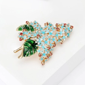 Detail of blue hydrangea brooch with enamel petals and gold leaf on a white pedestal