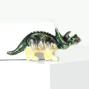Détail de la broche dinosaure tricératops vert brillant sur un support blanc