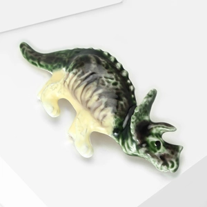 Vue macro d'une broche dinosaure tricératops en émail vert avec une texture brillante