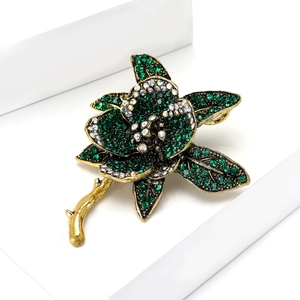 Close-up of vintage gold flower brooch with emerald green and iridescent white rhinestones