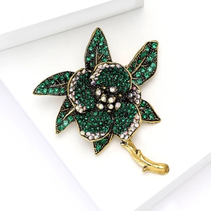 Elegant gold flower brooch with emerald green crystals on white geometric stand