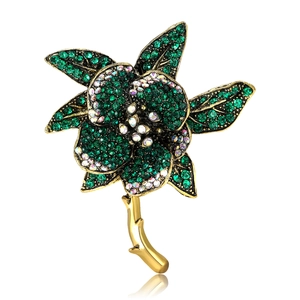 Luxurious flower brooch with green rhinestones and vintage gold finish on white background