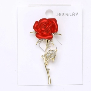 Détail d'une broche rose rouge avec feuilles dorées et cristaux sur une carte bijoux