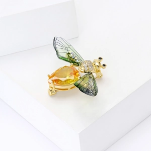 Macro shot of bee brooch with yellow pear gemstone and green enamel wings on white background