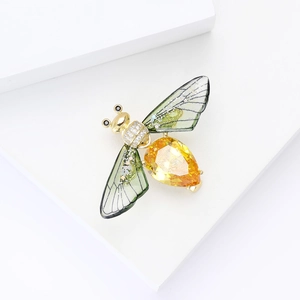 Detailed close-up of a luxury gold bee brooch with yellow crystal and green wings