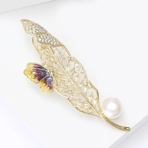 Détail d'une broche feuille avec cristaux, papillon coloré et perle blanche ronde