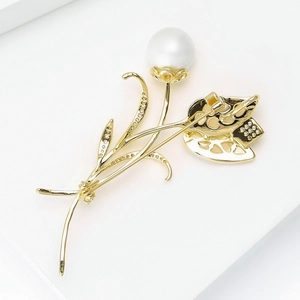 Détail d'une broche fleur dorée ornée d'une grande perle blanche et de finitions