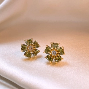 Macro shot of gold floral earrings with heart-shaped green crystals on silk fabric