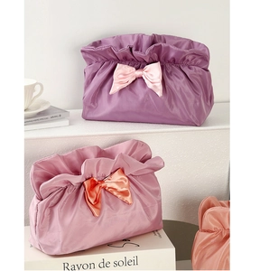Detail of the oversized bow decoration and soft pleated texture on satin makeup bags