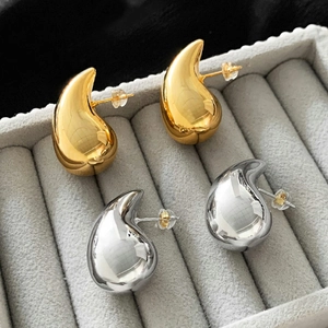 Macro shot of gold and silver teardrop earrings with mirror finish on grey velvet tray