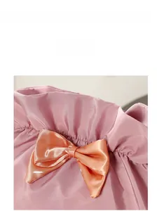 Close-up of pink satin makeup bag featuring a pleated design and bright orange bow detail