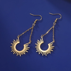 Détail de boucles d'oreilles dorées avec motif soleil et chaînes sur fond sombre