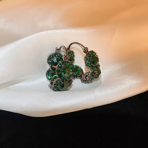 Detailed macro view of vintage emerald green stud earrings on white silk fabric