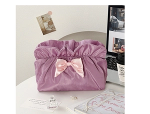 Flat lay of a lilac pleated makeup bag with a pink satin bow and luxury desk items