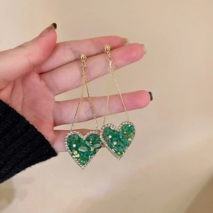 Close-up of vintage heart-shaped earrings with emerald green crystals and gold chains
