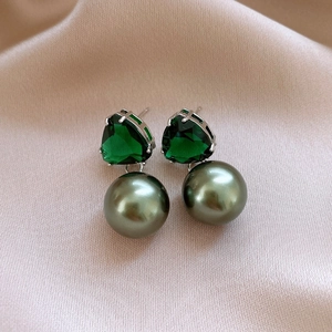 Detail of vintage emerald earrings with large dark green pearls on pink silk fabric