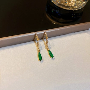 Detailed view of long gold drop earrings with emerald green pear-cut gems and zircons