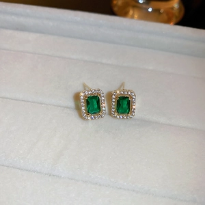 Macro shot of vintage emerald-cut green gemstone earrings with diamond halo in gold setting