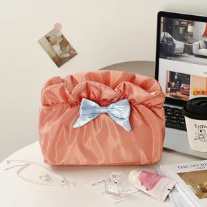 Pink drawstring makeup bag with blue ribbon bow on a stylish desk with accessories