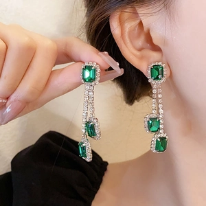 Close-up of emerald green tassel earrings with silver rhinestones on a female model