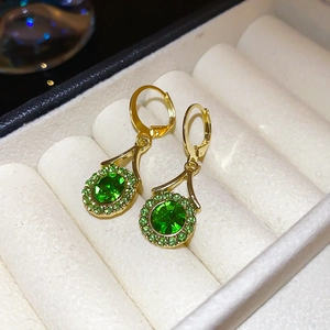 Macro view of emerald green oval stud earrings with diamonds in a white jewelry box