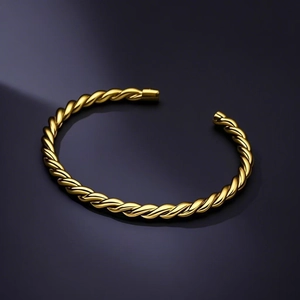 Detailansicht eines vergoldeten Edelstahl-Armreifens mit Zopfmuster auf dunklem Hintergrund.