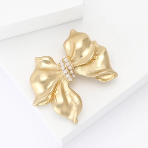Elegant matte gold alloy bow brooch with small white pearls on a minimalist white stage