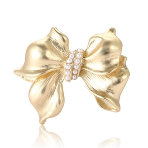 Elegant gold bow brooch with white pearls featuring a matte finish and mirror reflection