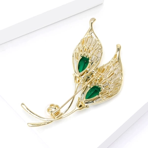 Detail of a luxury gold leaf brooch with emerald green stones and white pearl accent