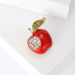 Broche pomme rouge avec feuilles en cristal vert et strass blancs sur fond blanc épuré