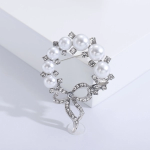Elegante spilla a corona in argento con perle bianche e fiocco di strass su base bianca