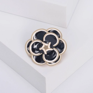 Detailed close-up of layered black and white enamel camellia brooch with gold metal edges