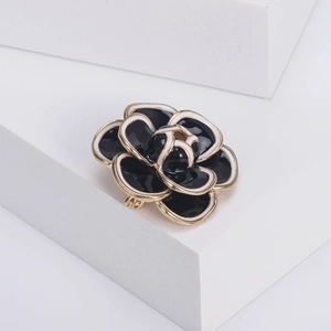 Macro shot of camellia brooch with black enamel petals and golden metal edges