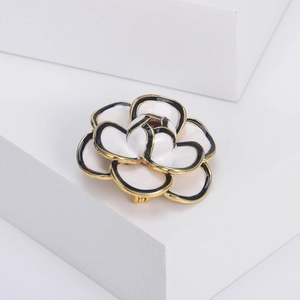 Detailed close-up of multilayered camellia brooch with white enamel and gold finish