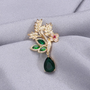 Détail d'une broche en forme de feuille dorée avec zircons et pierre goutte verte