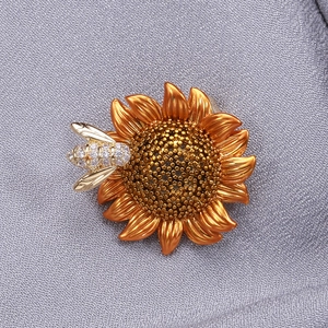 Macro detail of enamel sunflower brooch with zircon bee on grey fabric texture