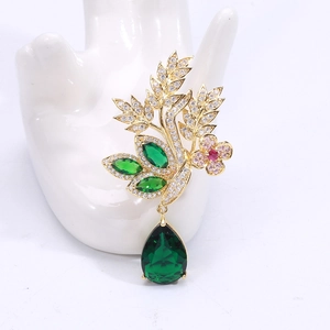 Détail d'une broche fleurie avec fleur rose et goutte de cristal vert sur support blanc
