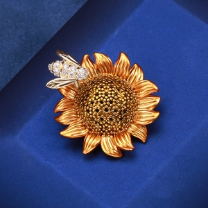 Detailed macro view of enamel sunflower brooch with sparkling zircon bee on a blue jewelry box