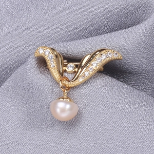 Elegant gold wing-shaped brooch with cubic zirconia and hanging pearl on gray fabric