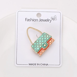 Detailed macro of a gold enamel quilted handbag brooch with green and orange finish