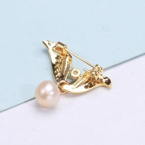 Detailed macro view of gold wing brooch with zircon stones and a round white pearl