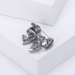 Gunmetal bow brooch with pearl detail and snowflake engraving on white geometric stand