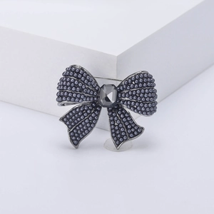 Elegant dark grey bow brooch with faux pearls and centerpiece gemstone on a stone display