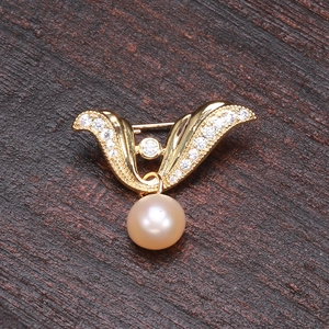 Golden wing pearl brooch with sparkling zircon inlays on a rustic wooden background